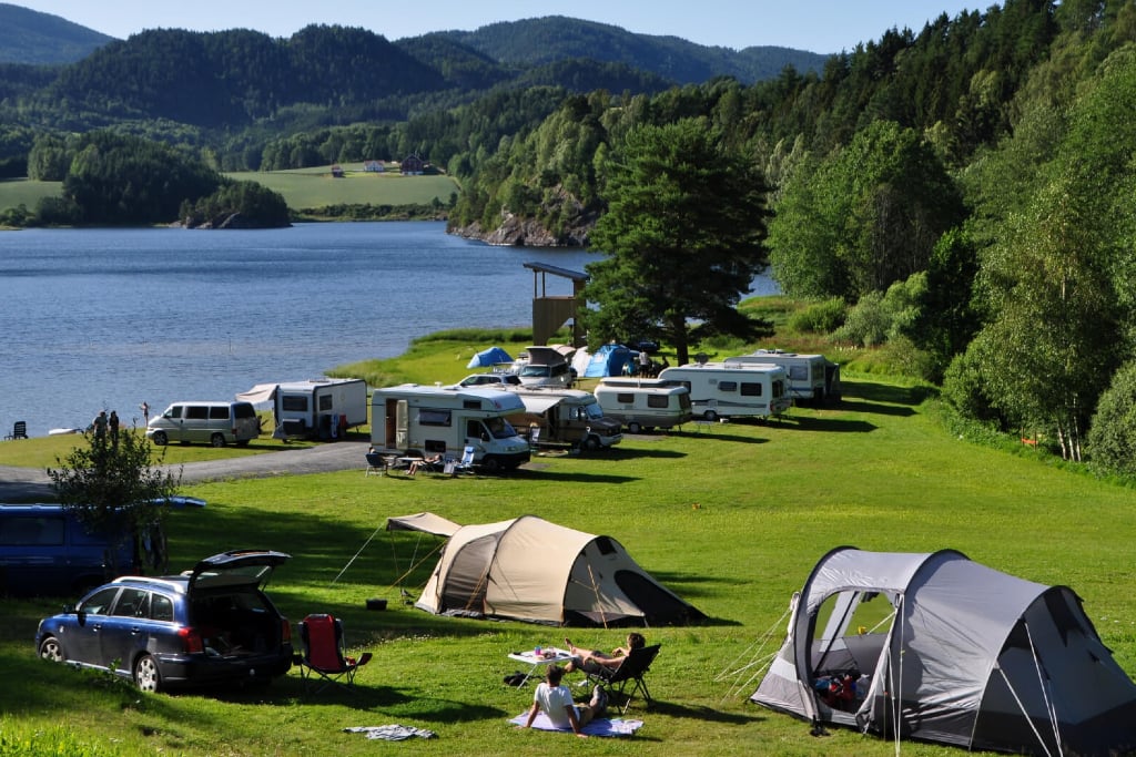 Telt og campingvogn ved innsjøen, omkranset av fjell og grønn natur, perfekt for campingopplevelser i Norge.