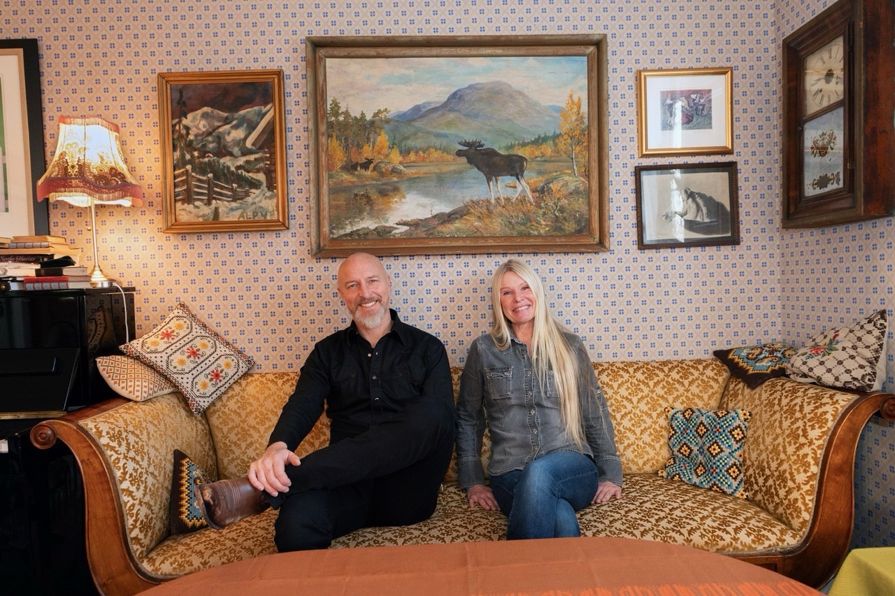 Par i vintage-stue med antikke malerier og møbler. Koselig atmosfære med fargerike puter og tapet.