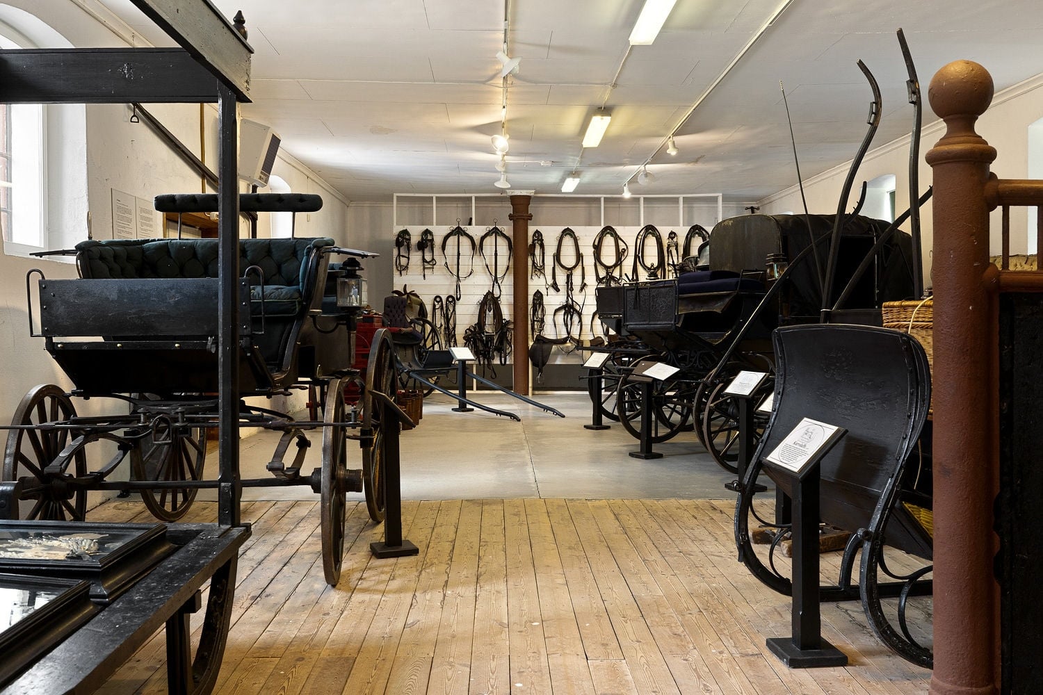 En visning av en hestevogn-utstilling med gamle sulkier og seletøy i muséet.