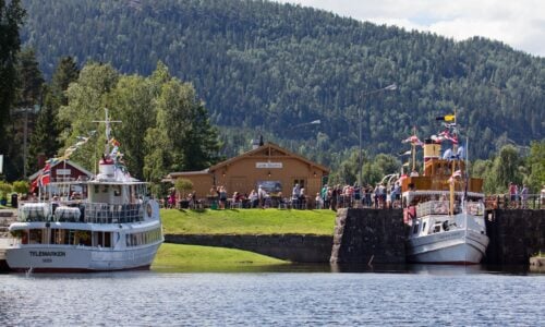 To båter i Lunde Sluser, med folk som nyter sommeren i naturskjønne omgivelser i Telemark.