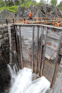 En syklist bærer sykkelen over slusene på Eidsfoss.