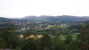 Utsikt over frodig dallandskap med hus og fjell i horisonten, sett fra en skogkledd høyde i Lunde.