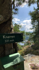 Knarren-fjellskilt ved 331 moh omringet av naturskjønn utsikt, trær og blå himmel. Perfekt turmål i Lunde.