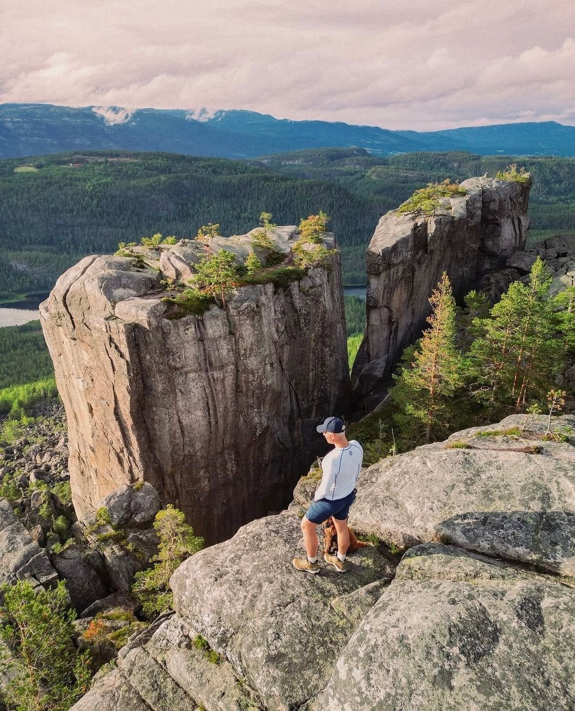 Mann på toppen av Gygrestolen, med utsikt over skog og fjell i solnedgangen.