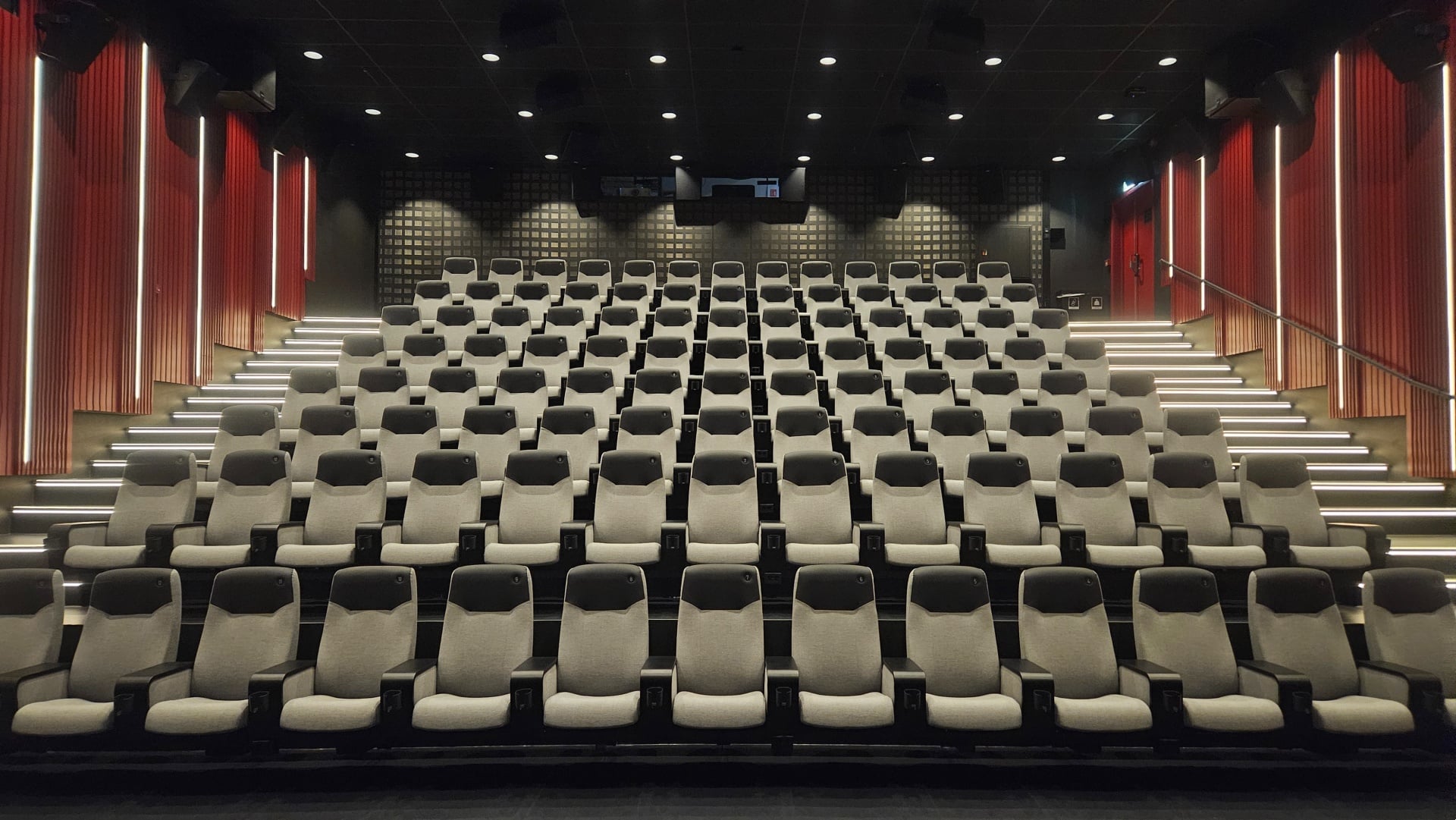 Moderne kinosal med rekke av komfortable seter i grått og røde vegger for en optimal filmopplevelse.