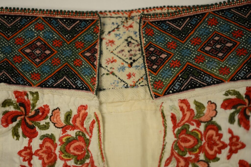 Detalj av tradisjonell norsk draktbroderi med fargerike mønstre og blomster, viser håndverkskunstritt.