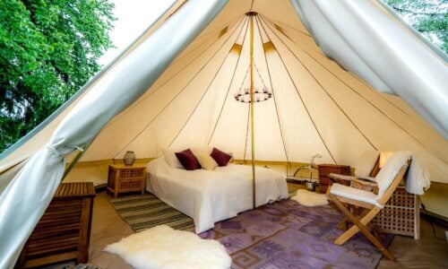 Glamping-teltinteriør med komfortabel seng, tepper og treinnredning i naturen. Foto