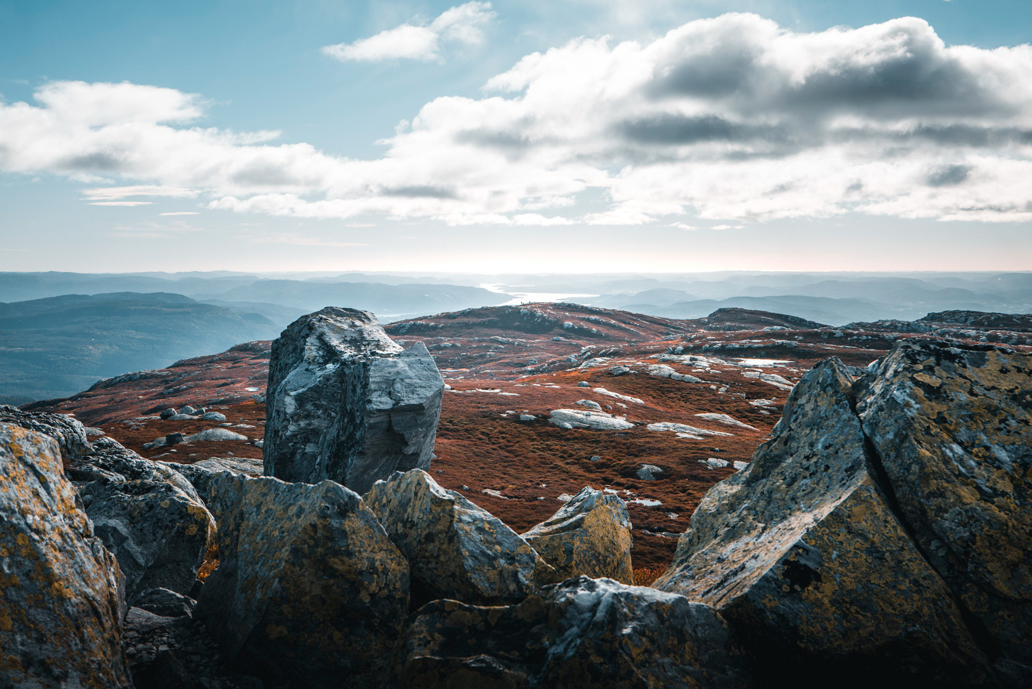Fjellandskap med steiner i forgrunnen og utsikt mot horisonten under en skyet himmel.