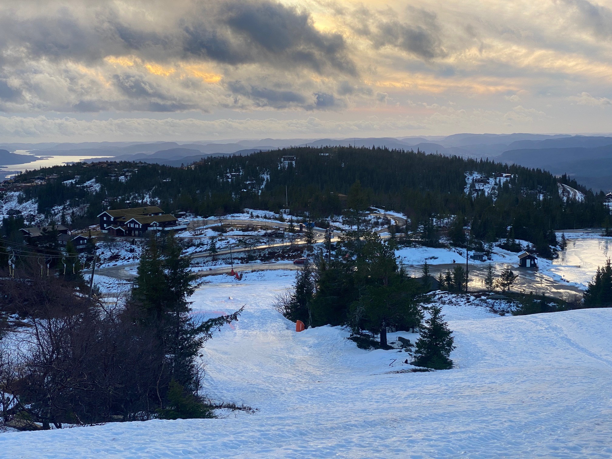 Snødekt landskap med hytter og skog under en dramatisk himmel i Norge.