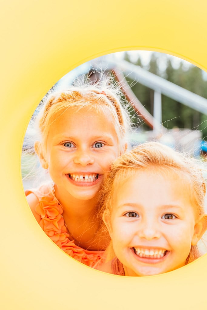 To flotte jenter smiler gjennom et gult hull, omfavnet av livlig lek og solfyllt glede. i Sommarland