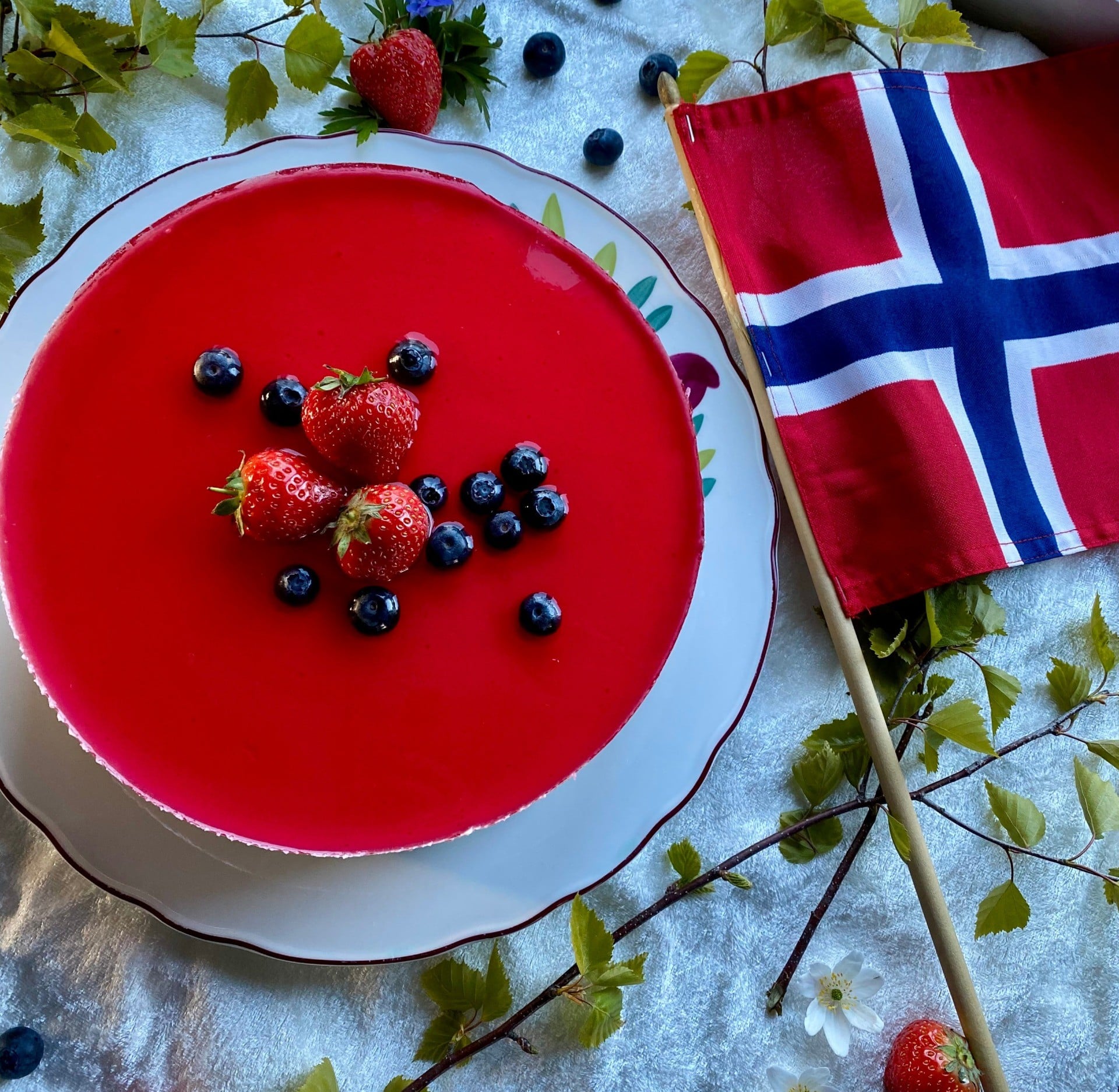 Flott rød bærkake med jordbær og blåbær, dekorert med det norske flagget og frisk grønn girlander.