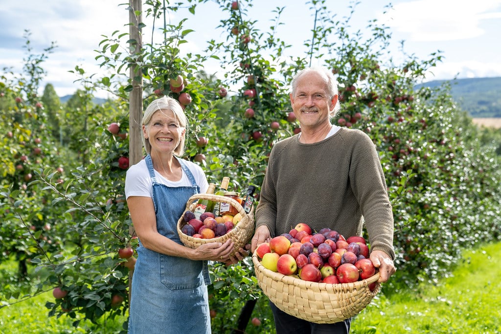 Par med epler i hagen, smilende og glade, med kurver fulle av ferske frukter om høsten.