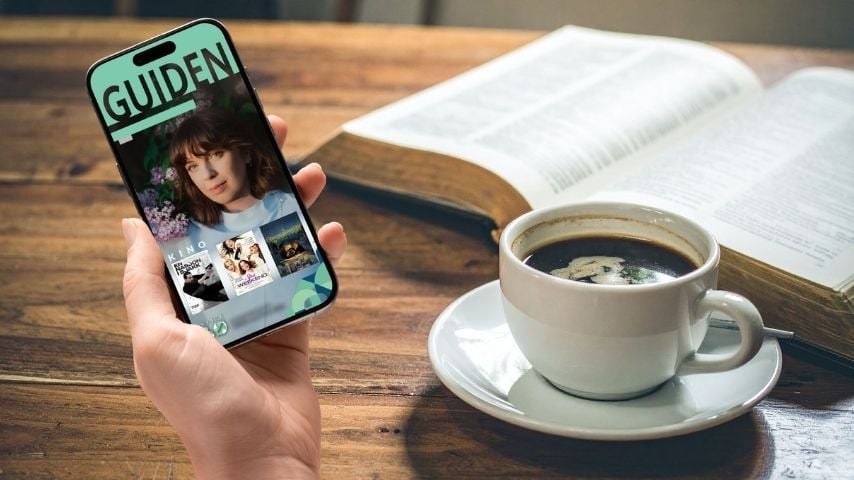 Mobiltelefon med kulturguide, kopp med kaffe og åpen bok på et trebord.
