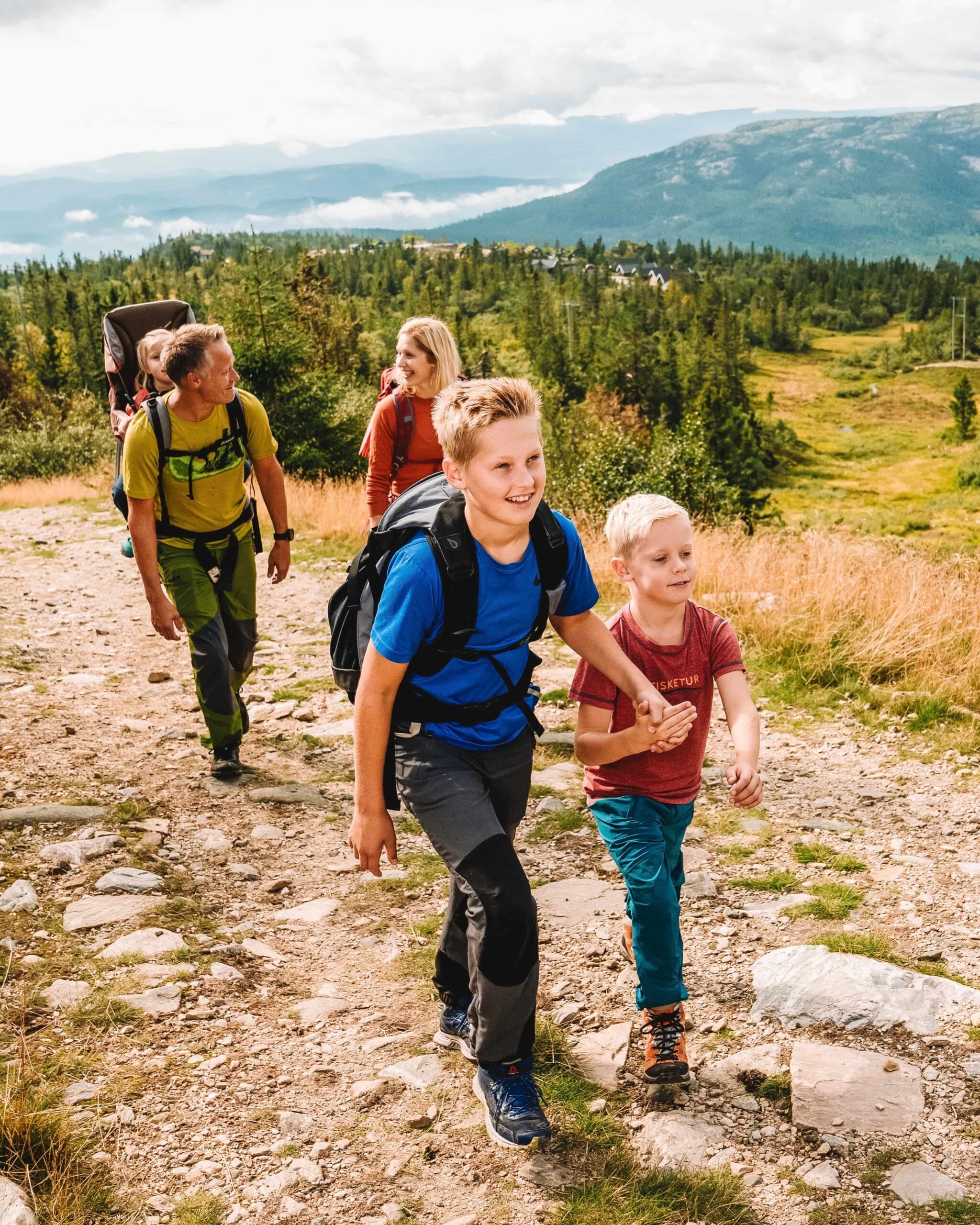 Familie på fottur i naturskjønt landskap med barn som er glade og aktive på stien.