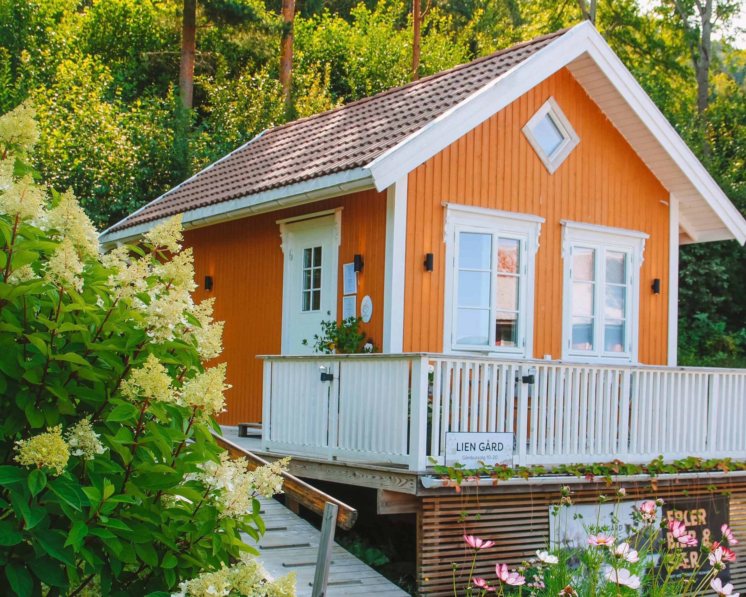 Sjarmerende oransje hytte med blomster og terrasse, omgitt av frodig natur og trær. Perfekt for utflukter.